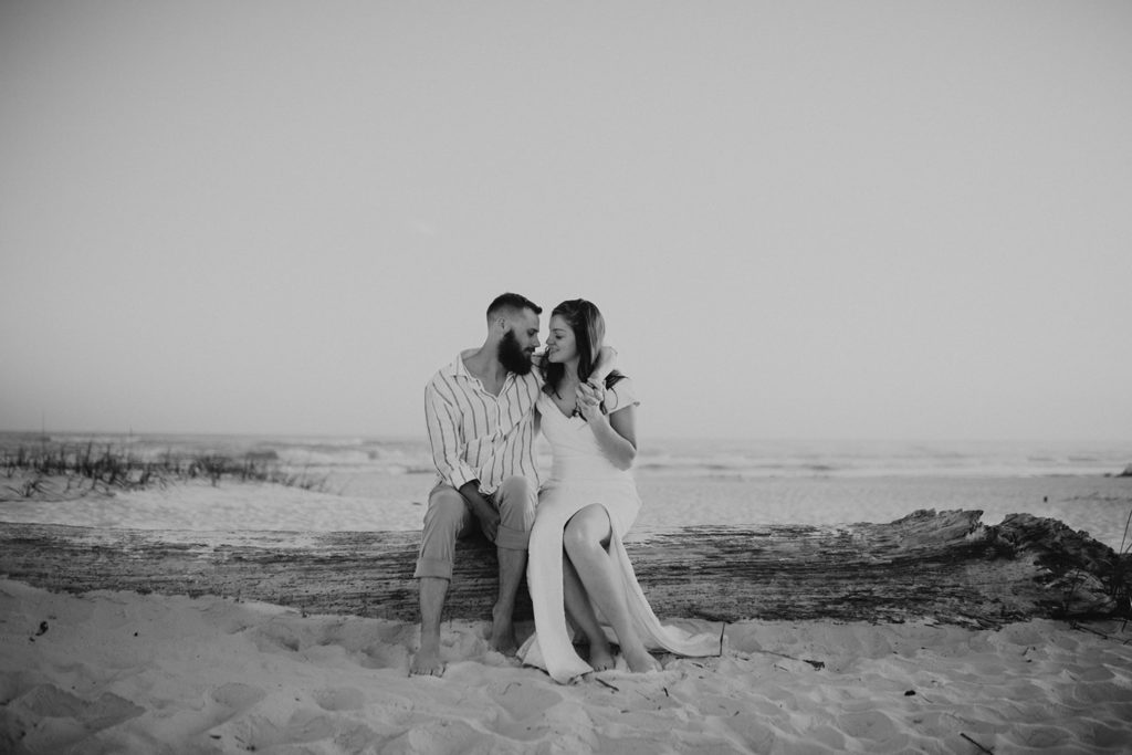 bride and groom sitting on driftwood on beach at Navarre Beach